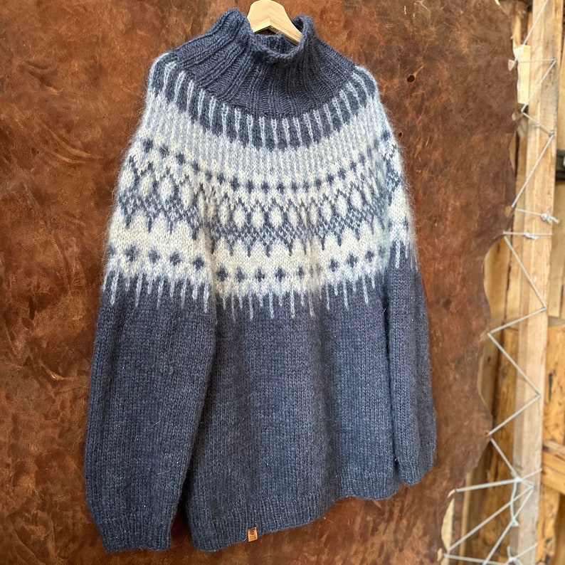 Puede incluir: Un su&eacute;ter de punto azul oscuro con un dise&ntilde;o estampado blanco y azul claro. El su&eacute;ter tiene cuello alto y mangas largas.