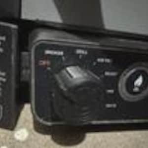 May include: A black control panel featuring a circular dial with settings labelled OFF, GRILL, and HIGH. To the right of the dial is a circular button with a white flame icon. Text on the left side provides instructions for the dial and switch.