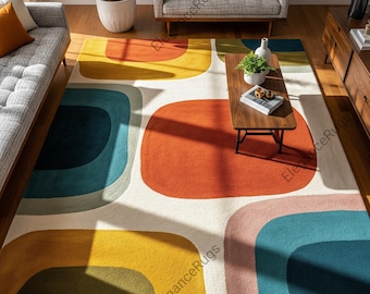 May include: A large, rectangular area rug with a retro design. The rug features large, rounded shapes in shades of orange, yellow, blue, and pink against a white background. The rug is placed in a living room setting with furniture.
