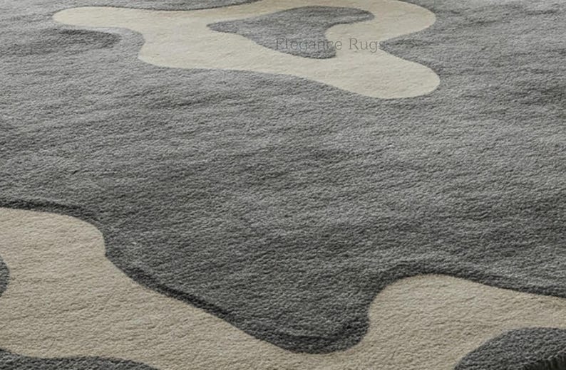K&ouml;nnte beinhalten: Nahaufnahme eines grauen und beigen Shaggy-Teppichs mit modernem, abstraktem Design. Der Teppich hat eine weiche, pl&uuml;schige Textur.