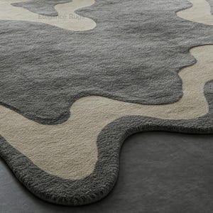 K&ouml;nnte beinhalten: Nahaufnahme eines grauen und cremefarbenen Teppichs mit einem welligen, abstrakten Design. Der Teppich hat eine weiche, pl&uuml;schige Textur.