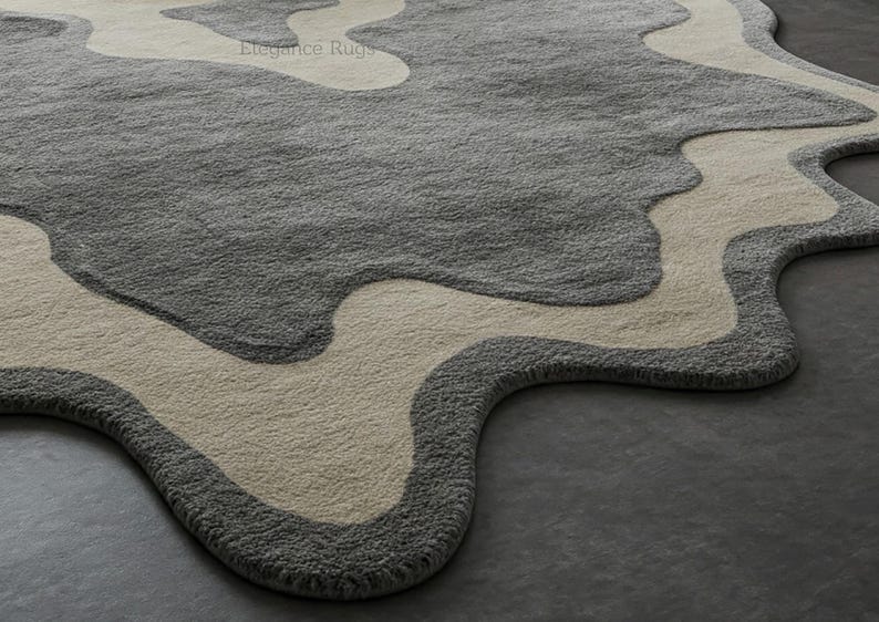 K&ouml;nnte beinhalten: Nahaufnahme eines grauen und cremefarbenen Teppichs mit einem welligen, abstrakten Design. Der Teppich hat eine weiche, pl&uuml;schige Textur.
