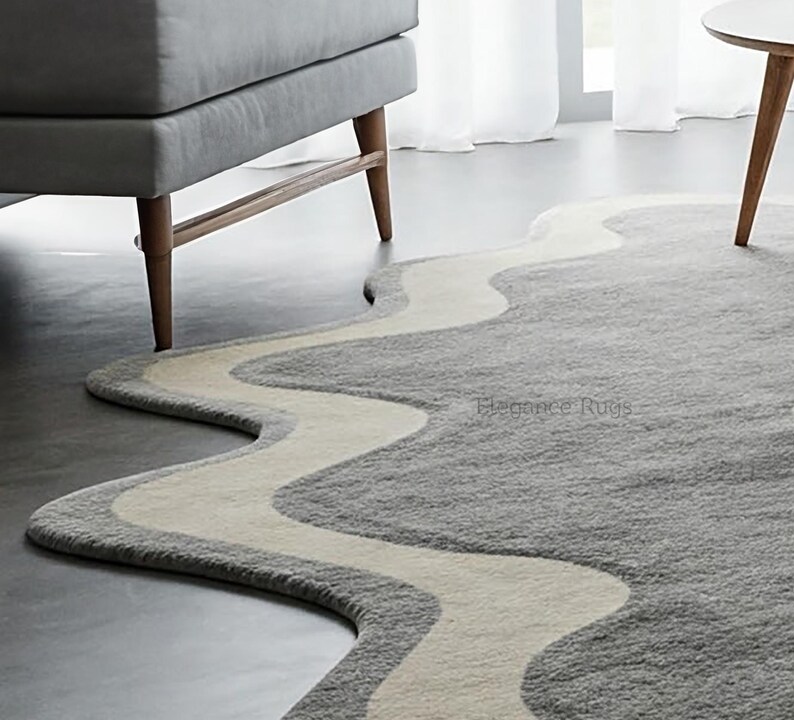 K&ouml;nnte beinhalten: Ein grauer und wei&szlig;er, wellenf&ouml;rmiger Teppich mit modernem Design. Der Teppich hat einen hellgrauen Hintergrund mit einer wei&szlig;en, wellenf&ouml;rmigen Linie, die durch die Mitte verl&auml;uft. Der Teppich ist aus einem weichen, pl&uuml;schigen Material gefertigt und perfekt, um jedem Raum einen Hauch von modernem Stil zu verleihen.