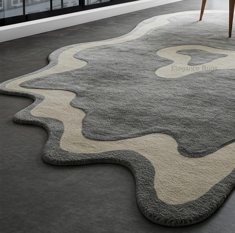 K&ouml;nnte beinhalten: Ein grauer und cremefarbener Teppich mit einem wellenf&ouml;rmigen, abstrakten Design. Der Teppich hat eine weiche, pl&uuml;schige Textur und ist aus hochwertigen Materialien gefertigt. Der Teppich ist perfekt, um jedem Raum einen Hauch von modernem Stil zu verleihen.