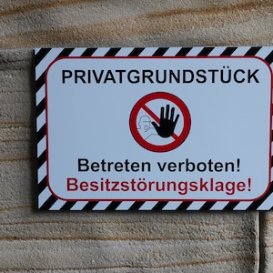 Könnte beinhalten: Ein weißes Schild mit schwarzen und roten Streifen um den Rand. Das Schild lautet "Privatgrundstück" und "Betreten verboten! Besitzstörungslage!" mit einem roten Kreis und einer durchgestrichenen Hand.