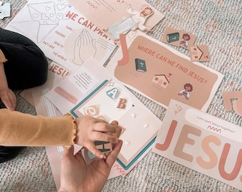 May include: Educational activity set with cards and puzzle pieces. The cards feature illustrations and text, including "Who is Jesus?" and "Where can we find Jesus?" A child's hand is interacting with the materials.