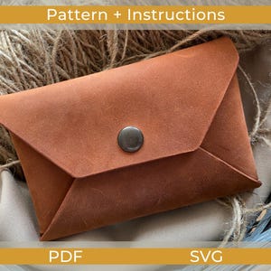 Könnte beinhalten: Eine braune Ledergeldbörse mit Druckknopfverschluss. Die Geldbörse hat ein gefaltetes Klappendesign und besteht aus einem strukturierten Material. Das Bild enthält auch den Text "Pattern + Instructions", "PDF" und "SVG".