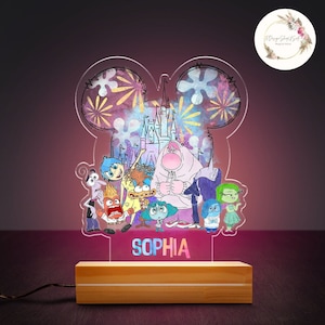 May include: A clear acrylic night light shaped like Mickey Mouse's head with a galaxy design and fireworks. The light features characters from the movie Inside Out, including Joy, Sadness, Anger, Fear, and Disgust. The light is personalized with the name "SOPHIA".