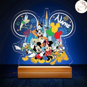 May include: A personalized Disney-themed night light featuring Mickey Mouse, Minnie Mouse, Donald Duck, Goofy, Pluto, and Tinkerbell. The light is shaped like Mickey Mouse's ears and has a wooden base. The text "NAME" is included in the design.