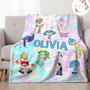 May include: A soft, blue and pink fleece blanket with a colorful cartoon design featuring characters from the movie Inside Out. The blanket has the name "Olivia" printed in blue letters.