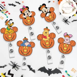 May include: A selection of Halloween-themed retractable badge holders featuring Disney characters. Each holder shows a character such as Mickey Mouse or Winnie the Pooh inside an orange pumpkin. The holders have a white reel and a clear plastic strap.