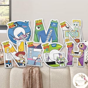 May include: A collection of colorful Toy Story-themed letter pillows. Each letter features a different character and name, including "Quinn," "Madison," "Natalie," "Nancy," "Emily," "Grace," and "Hannah." The pillows are displayed on a beige sofa.
