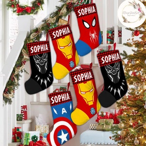 May include: Six red and black Christmas stockings with a white buffalo plaid trim. Each stocking has a different superhero character on it: Iron Man, Spider-Man, Black Panther, and Captain America. The stockings are personalized with the name "Sophia" on each one.