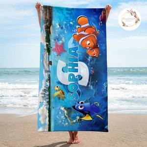 May include: A blue beach towel with a Finding Nemo theme. The towel features Marlin and Dory, a turtle, and a starfish. The name "Sophia" is written in large letters on the towel.