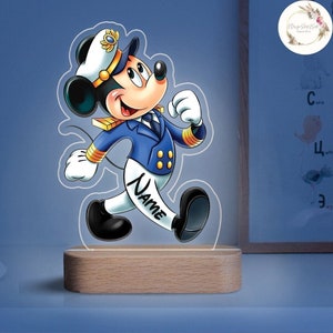 May include: A decorative night light featuring a cartoon mouse character in a navy blue captain's uniform. The mouse is walking with a smiling expression. The base is made of light-colored wood, and the name "NAME" is written on the pants.