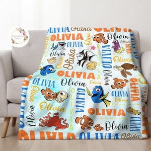 May include: A blue and orange fleece blanket with a Finding Nemo theme. The blanket features the characters Dory, Marlin, Nemo, and other sea creatures. The name "Olivia" is repeated throughout the blanket.