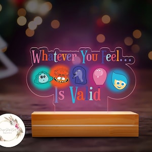 May include: A wooden base with a clear acrylic light-up sign featuring the characters from the movie Inside Out. The sign reads "Whatever You Feel... Is Valid".