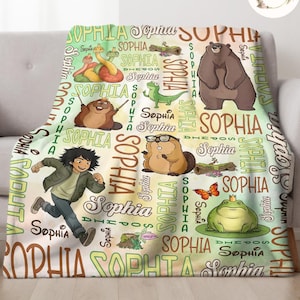 May include: A personalized fleece blanket featuring the name "Sophia" in various fonts and sizes. The blanket showcases cartoon illustrations of a bear, frog, snake, and other animals. The color palette includes shades of green, brown, and orange.