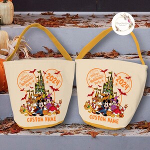 May include: Two beige canvas trick-or-treat bags with yellow handles. The bags feature a Mickey Mouse Halloween party design with Mickey Mouse, Minnie Mouse, Goofy, Donald Duck, and Pluto. The bags also feature the text "Mickey's Not-So-Scary Halloween Party" and "2024".