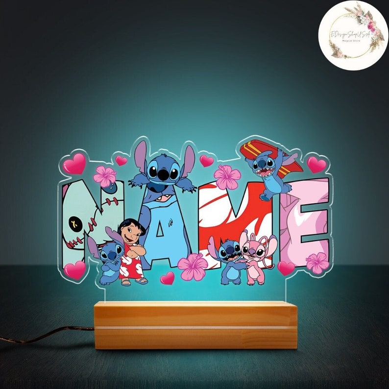 May include: A light-up name sign with the word "NAME" in blue, pink, and red. The letters are decorated with Stitch and Angel characters from the Disney movie Lilo & Stitch. The sign is on a wooden base.
