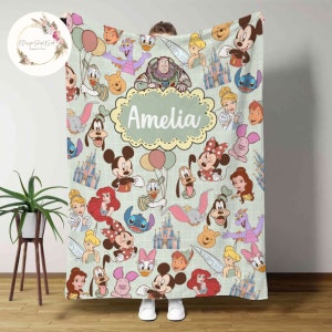 May include: A green fleece blanket with a colorful pattern of Disney characters, including Mickey Mouse, Minnie Mouse, Donald Duck, Goofy, and more. The blanket has a personalized name, "Amelia", in a yellow oval.