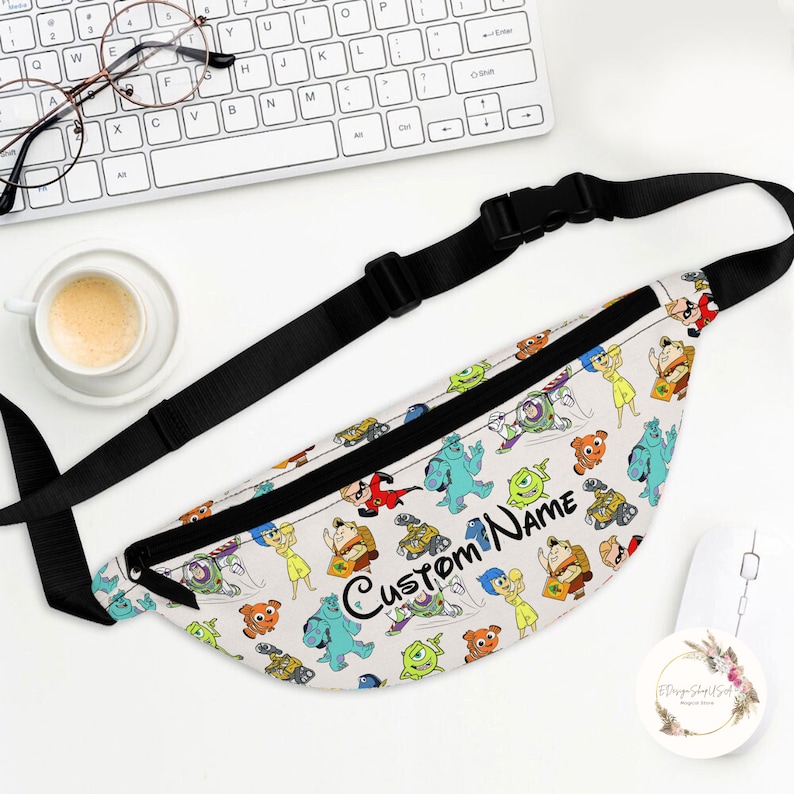 Puede incluir: Una ri&ntilde;onera blanca con una correa negra. La ri&ntilde;onera tiene un estampado colorido de varios personajes de Disney Pixar, incluidos Buzz Lightyear, Woody, Sulley, Mike Wazowski y muchos m&aacute;s. El texto "Custom Name" est&aacute; impreso en negro en la parte delantera de la ri&ntilde;onera.