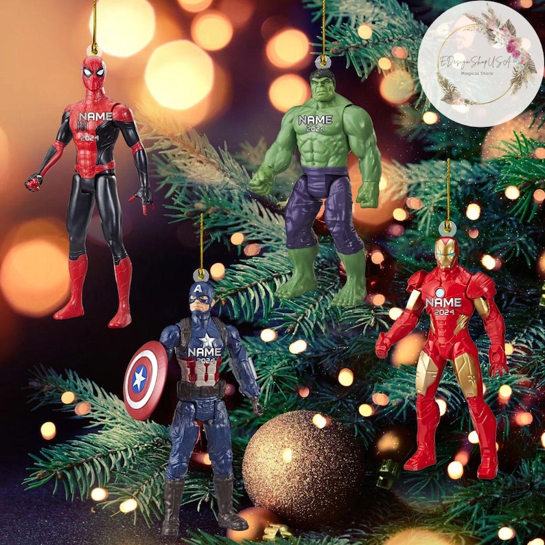 K&ouml;nnte beinhalten: Vier Superhelden-Weihnachtsbaumschmuck mit Spiderman, Hulk, Captain America und Iron Man. Jeder Schmuck ist eine rote, gr&uuml;ne, blaue oder rote Figur mit einem Namensschild, auf dem "NAME 2024" steht.