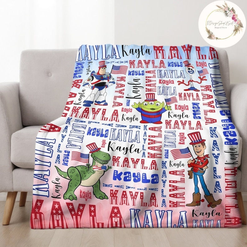Puede incluir: Una manta de franela suave, azul y rosa con un tema patri&oacute;tico. La manta presenta un patr&oacute;n repetido del nombre "Kayla" e im&aacute;genes de personajes de Toy Story, incluidos Buzz Lightyear, Woody, Rex y Alien. Los personajes llevan sombreros patri&oacute;ticos rojo, blanco y azul.
