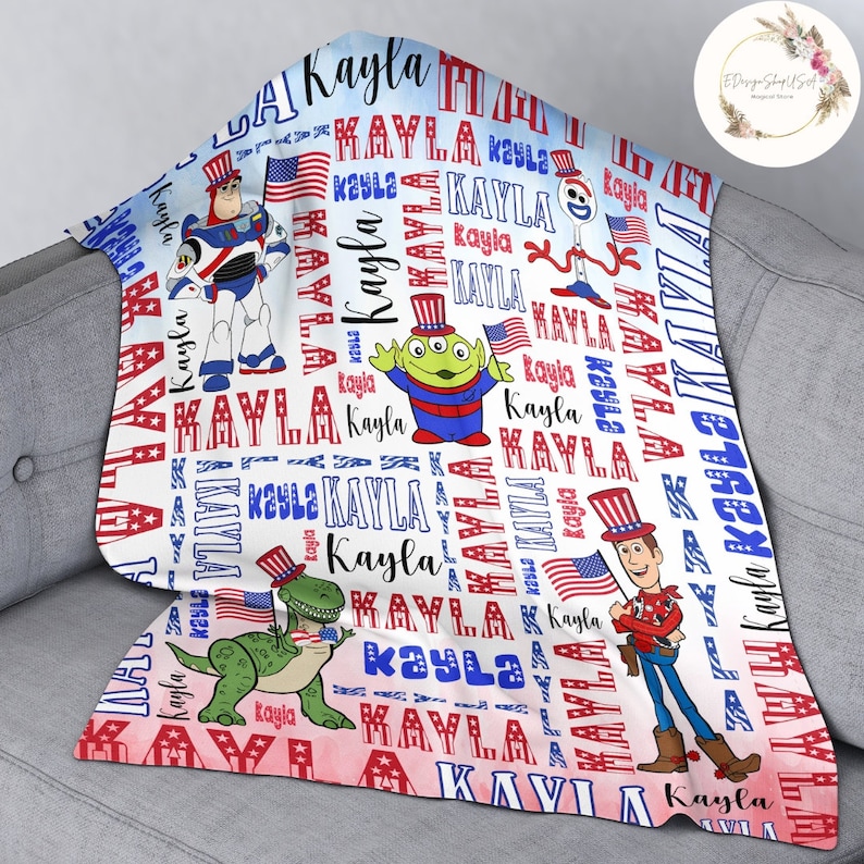 Puede incluir: Una manta de beb&eacute; blanca con un tema patri&oacute;tico rojo, blanco y azul. La manta presenta el nombre "Kayla" repetido en todo el dise&ntilde;o, junto con im&aacute;genes de personajes de Toy Story con sombreros patri&oacute;ticos.
