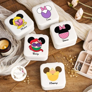 May include: Five white square jewelry boxes with different Disney princess characters on the lids. The boxes are arranged in a semi-circle on a wooden surface. The names "Michelle", "Carol", "Donna", "Betty", and "Kimberly" are printed on the boxes.