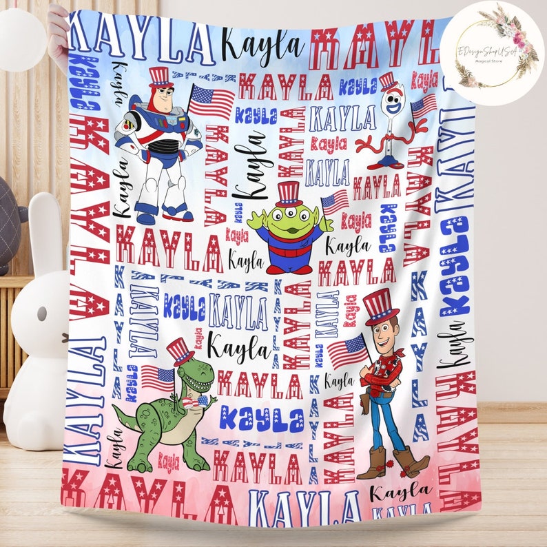 Puede incluir: Una manta de beb&eacute; blanca con un tema patri&oacute;tico rojo, blanco y azul. La manta presenta el nombre "Kayla" repetido en todo el dise&ntilde;o, junto con im&aacute;genes de personajes de Toy Story con sombreros patri&oacute;ticos. Los personajes incluyen a Woody, Buzz Lightyear, Rex y Alien.