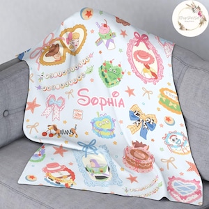 May include: A light blue baby blanket with a repeating pattern of Toy Story characters, stars, and bows. The blanket features the name "Sophia" in a pink and white font.