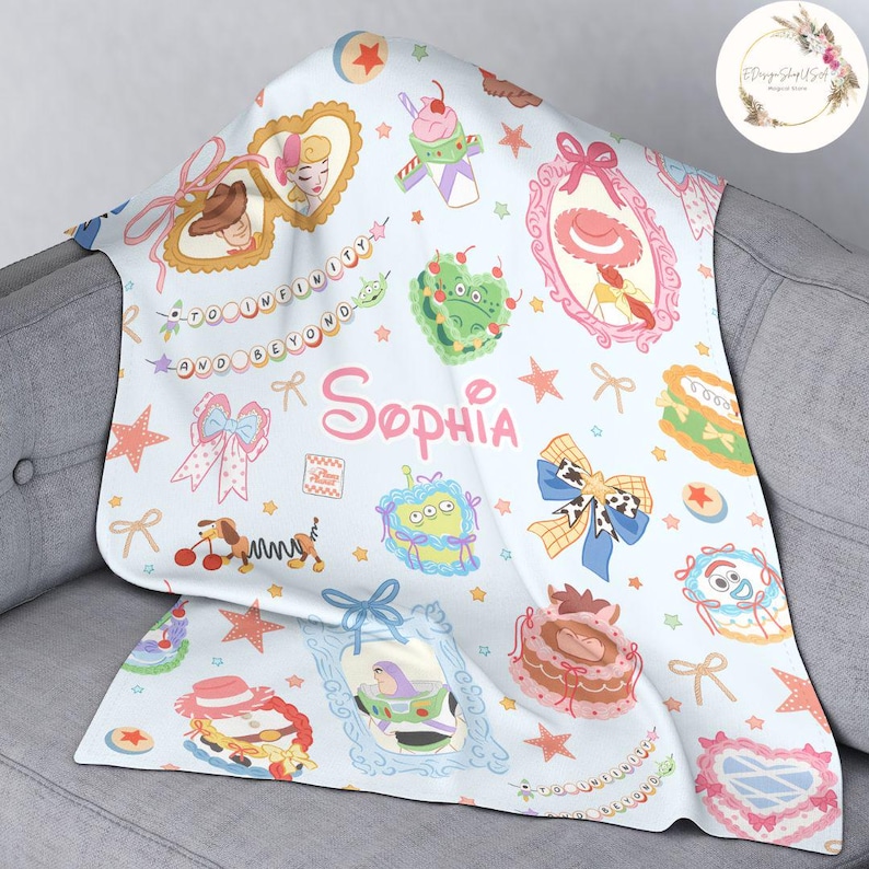 May include: A light blue baby blanket with a repeating pattern of Toy Story characters, stars, and bows. The blanket features the name "Sophia" in a pink and white font.