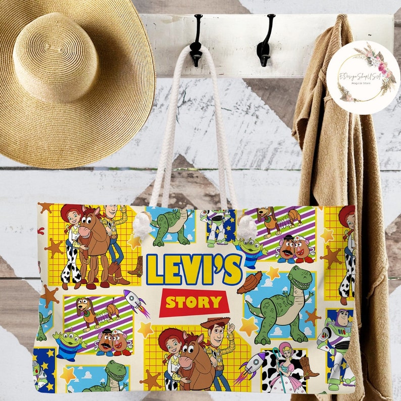以下が含まれることがあります： おもちゃのストーリー映画フランチャイズのキャラクターが描かれたカラフルなデザインの白いキャンバス地のトートバッグ。バッグには白いロープのハンドルと、前面に「Levi's Story」という文字が印刷されています。