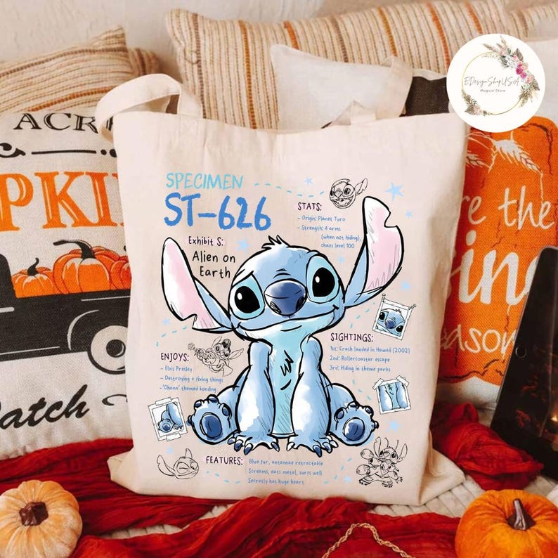 May include: Off-white canvas tote bag featuring a blue cartoon alien character, with the text "SPECIMEN ST-626" and "Alien on Earth". The bag includes illustrations and text detailing the character's stats, sightings, and features.