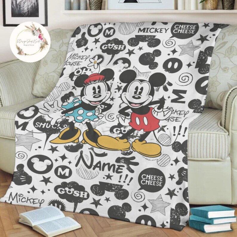 Może przedstawiać: Biały koc z polaru z czarno-białym wzorem bazgroł&oacute;w przedstawiającym Myszki Miki i Minnie. Wz&oacute;r zawiera słowa "Mickey Mouse", "Gush", "Cheese Cheese", "Name" i "Shucks".