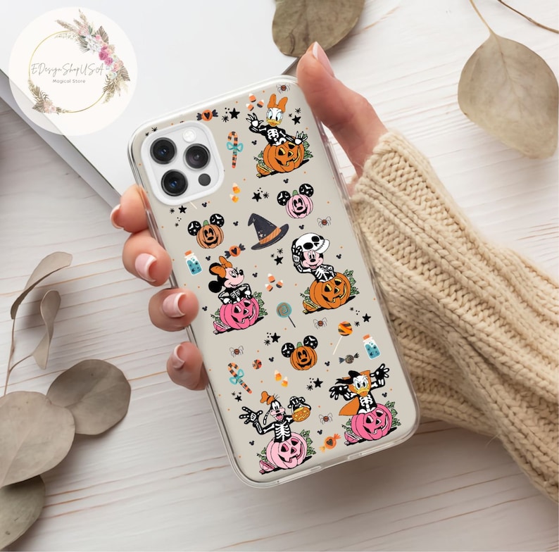 May include: Clear phone case with a Halloween-themed design featuring Mickey Mouse, Minnie Mouse, Donald Duck, and Goofy dressed in costumes and pumpkins. The case has a white background with black, orange, and pink accents.