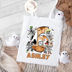 Puede incluir: Bolsa de tela blanca con un dise&ntilde;o de tem&aacute;tica de Halloween con personajes de la franquicia Toy Story. El dise&ntilde;o incluye un gran n&uacute;mero 5 naranja, una telara&ntilde;a y personajes vestidos de esqueletos. El texto "ASHLEY" est&aacute; impreso debajo del dise&ntilde;o.
