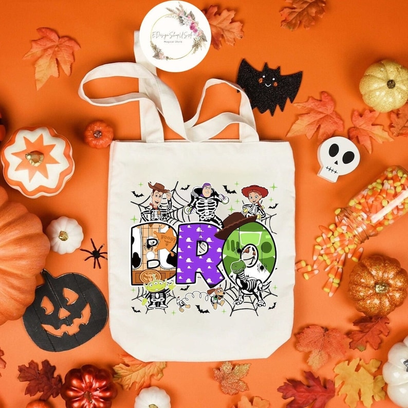Puede incluir: Una bolsa de lona blanca con un gr&aacute;fico colorido de los personajes de Toy Story, Woody, Buzz Lightyear y Jessie. Los personajes est&aacute;n dispuestos para deletrear la palabra "BRO" con un dise&ntilde;o de telara&ntilde;a en el fondo.