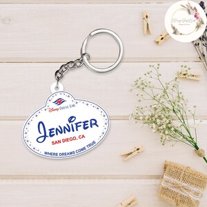 May include: White oval-shaped keychain with a blue and red Disney Cruise Line logo, the text "JENNIFER", "SAN DIEGO, CA", and "WHERE DREAMS COME TRUE".