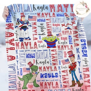 Puede incluir: Una manta blanca con un patr&oacute;n rojo, blanco y azul con los nombres "Kayla" y "MAYLA" repetidos a lo largo de la misma. La manta tambi&eacute;n presenta im&aacute;genes de personajes de Toy Story, incluyendo Woody, Buzz Lightyear, Rex y Alien.