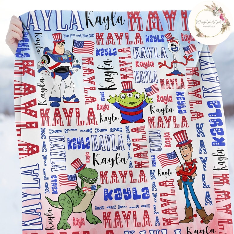 Puede incluir: Una manta blanca con un patr&oacute;n rojo, blanco y azul con los nombres "Kayla" y "MAYLA" repetidos a lo largo de la misma. La manta tambi&eacute;n presenta im&aacute;genes de personajes de Toy Story, incluyendo Woody, Buzz Lightyear, Rex y Alien.