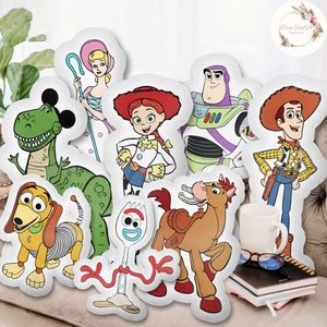 Op de afbeelding: Een set van negen pluche kussens met personages uit de Toy Story-franchise. De personages zijn Woody, Buzz Lightyear, Jessie, Rex, Slinky Dog, Forky, Bullseye, Bo Peep en een groene dinosaurus.