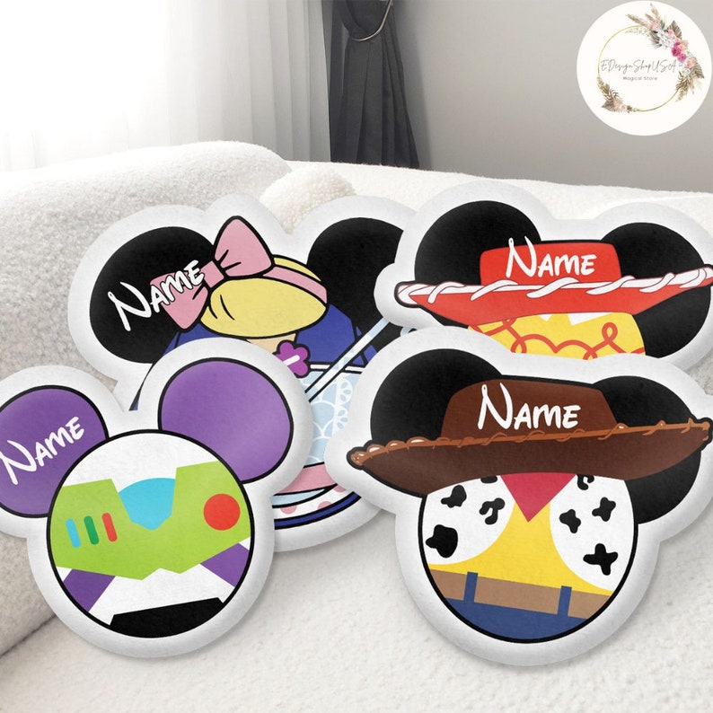 K&ouml;nnte beinhalten: Vier wei&szlig;e Kissenbez&uuml;ge mit gestickten Gesichtern von Disney-Charakteren. Jeder Kissenbezug hat ein schwarzes Mickey-Mouse-Ohren-Design und das Wort "Name" ist auf den Bezug gestickt. Die Charaktere sind Woody, Buzz Lightyear, Jessie und ein Charakter aus Toy Story 4.