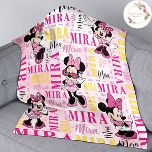 Puede incluir: Manta personalizada rosa y amarilla con tem&aacute;tica de Minnie Mouse. La manta presenta un patr&oacute;n repetido del nombre "Mira" y im&aacute;genes de Minnie Mouse con un vestido de lunares y gafas de sol.