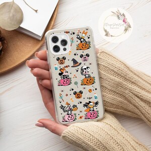 May include: A clear phone case with a Halloween-themed design featuring Mickey Mouse, Minnie Mouse, Donald Duck, and Goofy dressed in costumes. The case has a white background with orange, black, and pink accents. The characters are surrounded by pumpkins, sweets, and stars.