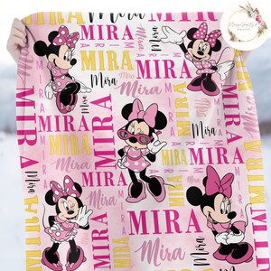 Puede incluir: Manta personalizada rosa y amarilla con un patr&oacute;n repetido de Minnie Mouse, la novia de Mickey Mouse. La manta presenta el nombre "Mira" repetido en todo el dise&ntilde;o.