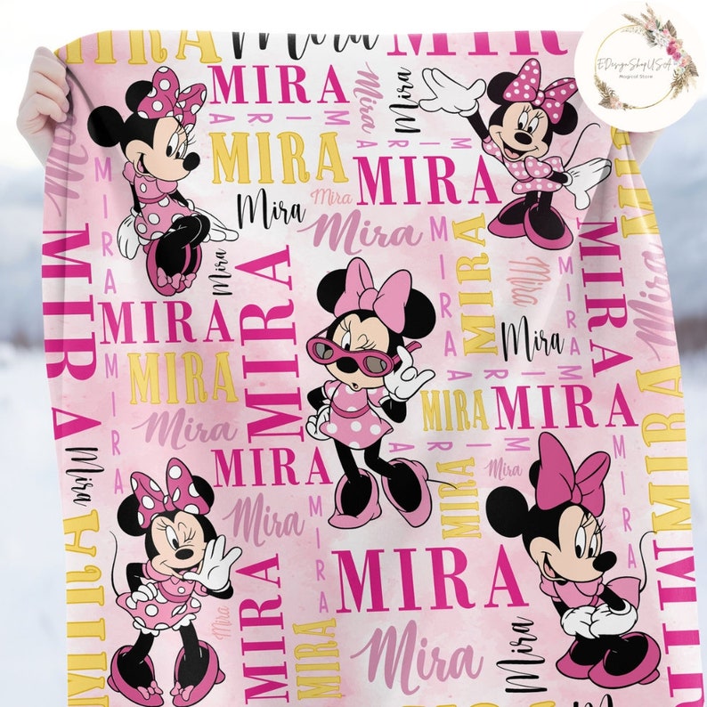 Puede incluir: Manta personalizada rosa y amarilla con un patr&oacute;n repetido de Minnie Mouse, la novia de Mickey Mouse. La manta presenta el nombre "Mira" repetido en todo el dise&ntilde;o.