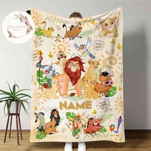 May include: A cream-colored fleece blanket with a colorful illustration of characters from the Lion King movie. The blanket features Simba, Nala, Pumbaa, Timon, and other characters. The text "Hakuna Matata" is repeated throughout the blanket. The blanket also includes the word "NAME" in a large font.