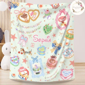 May include: A green and pink baby blanket with a Toy Story theme. The blanket features characters from the movie, including Woody, Buzz Lightyear, and Jessie. The blanket also has a personalized name, "Sophia", in a pink font.